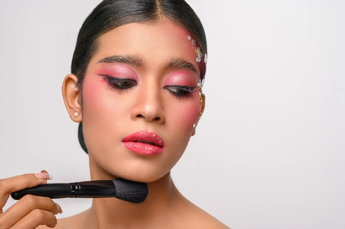 Frau mit rosa Make-up, die einen Rougepinsel hält, freigestellt vor weißem Hintergrund.